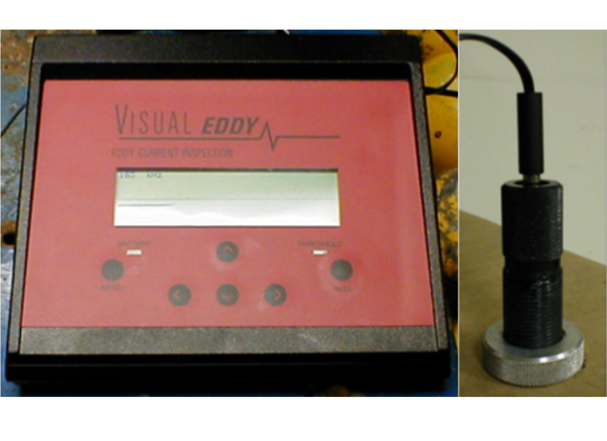 Eddy Current Equipment showing the main controller on the left and the probe to the right. The probe is a black cylinder about two inches long with a wider metal knob on the top and a cord at the back.