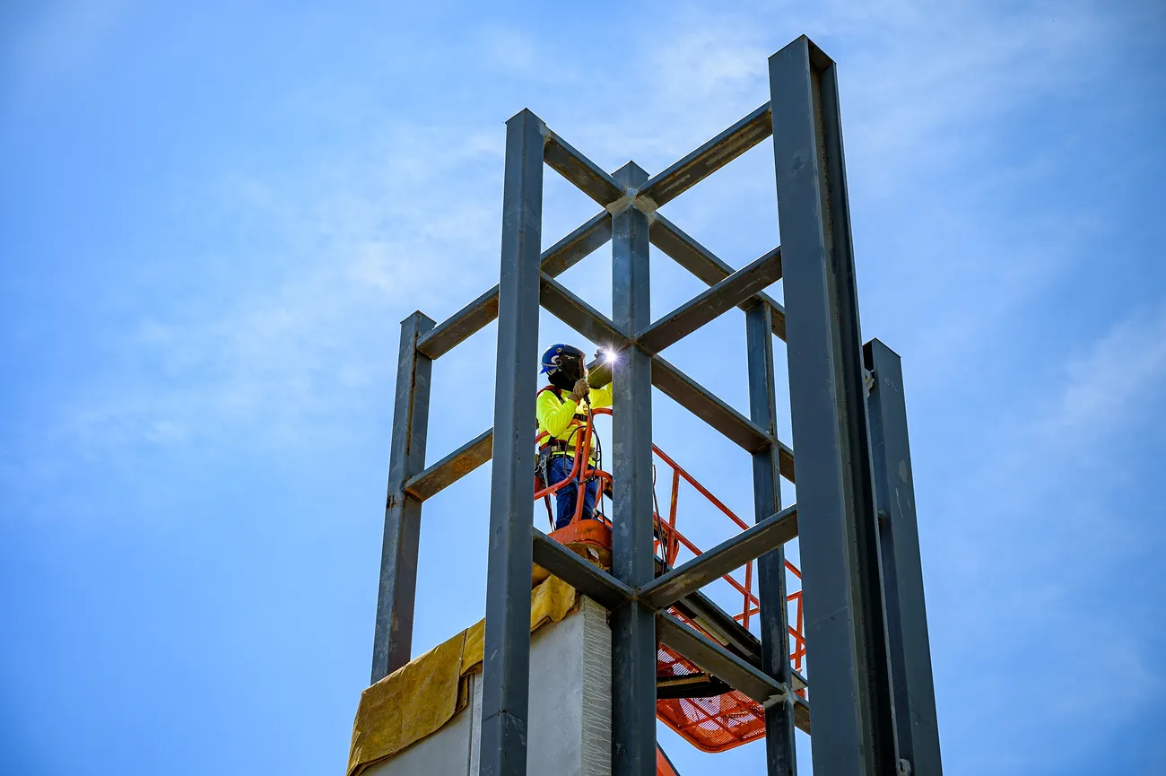 A construction worker welds steel building connections while standing in an aerial work platform.