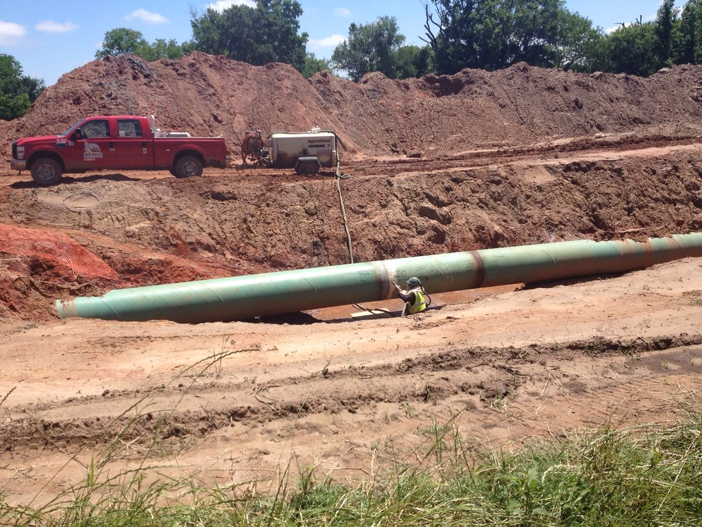 A pipeliner works on a cross-country pipe, with the work truck and trailered welding machine in the background.