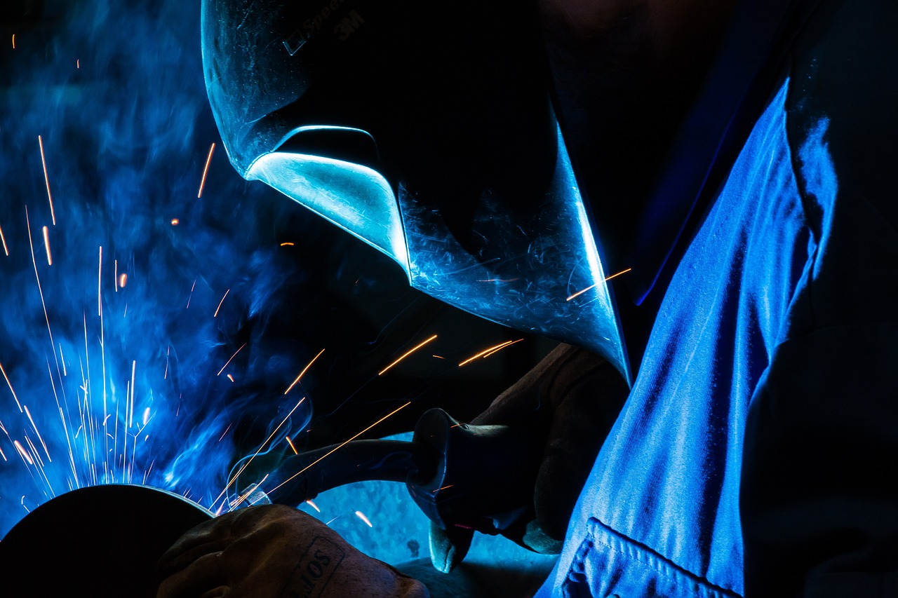 A welder wearing a welding hood and coveralls uses GMAW