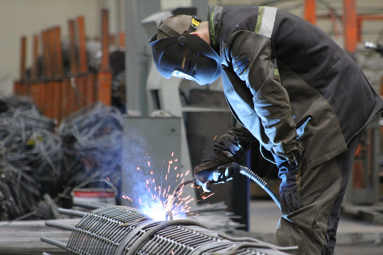 A man welds rebar with a wire feed welder, his clothes illuminated by the welding arc.