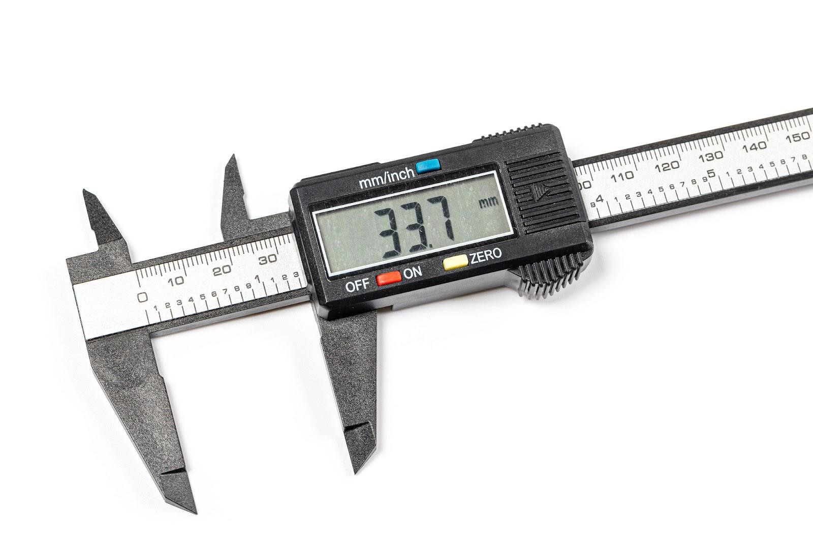 A photograph of a set of digital calipers showing the bar with Imperial and metric scales, the outside and inside jaws, and the digital indicator attached to the sliding lower jaws. The calipers are open, and the digital display reads 33.7 milimeters.