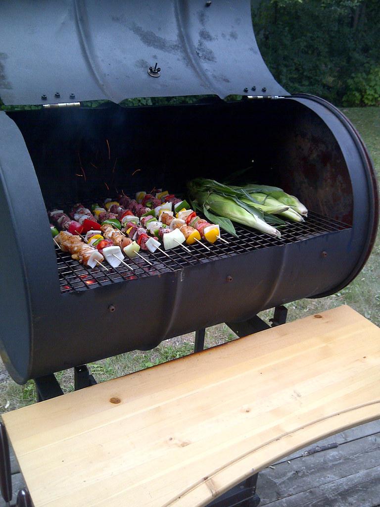 A grill made from a 55-gallon drum has its lid open, revealing food being cooked.