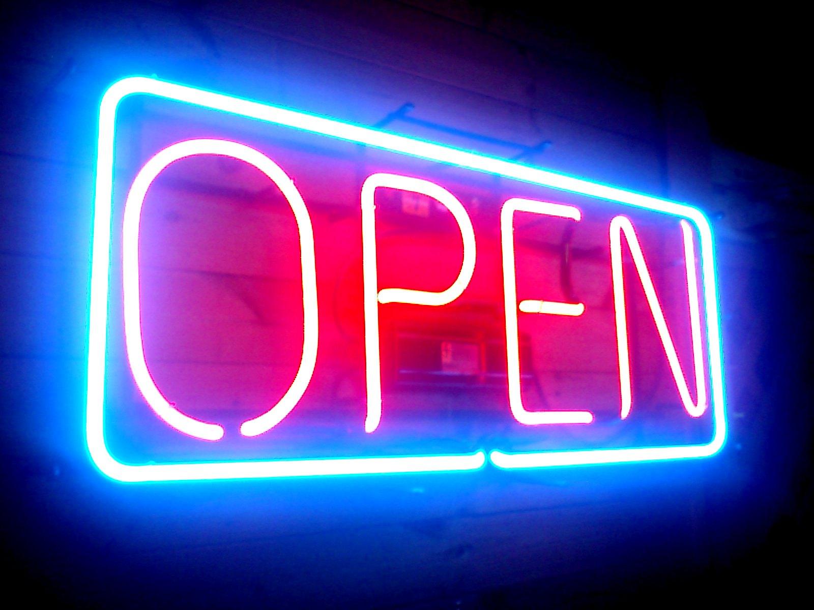 A fluorescent sign that says open in red letters surrounded by a blue border.