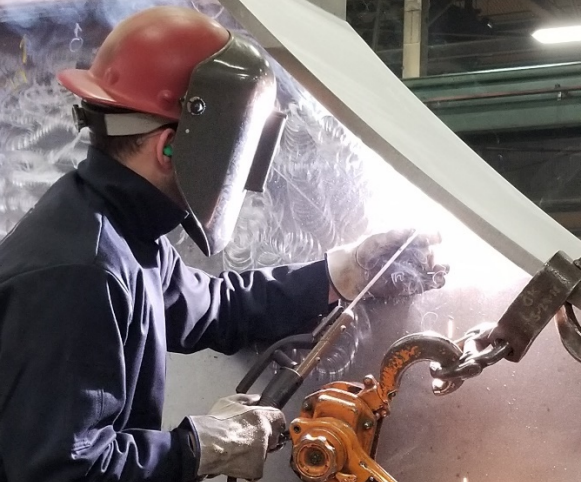 A welder uses SMAW to weld a flange onto a large structural member.