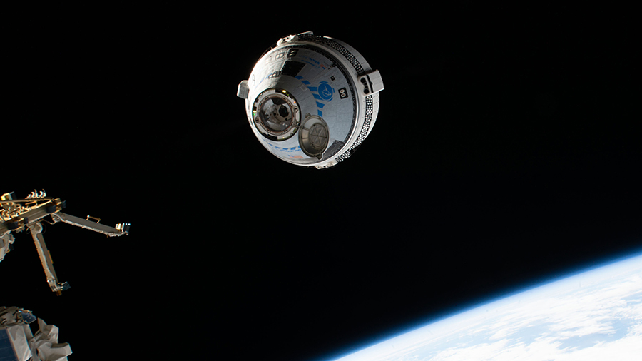 a crew capsule in space. On the lower right, Earth is pictured. The capsule is cylindrical with a cone-shaped front. To the left, and slightly out of frame, is the International Space Station prepping to accept the crew capsule.