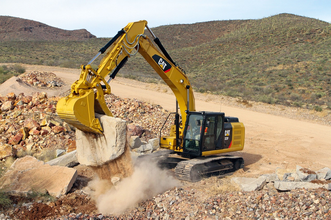 An excavator with a claw attachment pics up a large boulder.