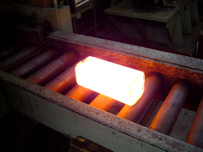 Hot Ingot, which is shaped like a brick but glowing bright orange with heat. The ingot moves down a conveyer belt into the roller mechanism.