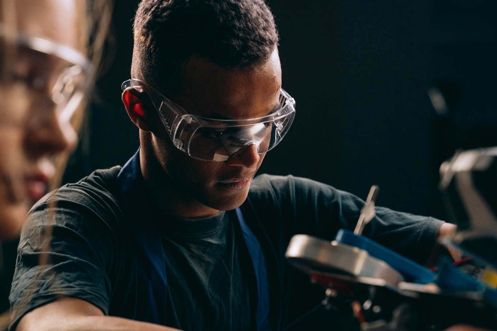 Two shop workers wear safety glasses while using hand tools in a shop.