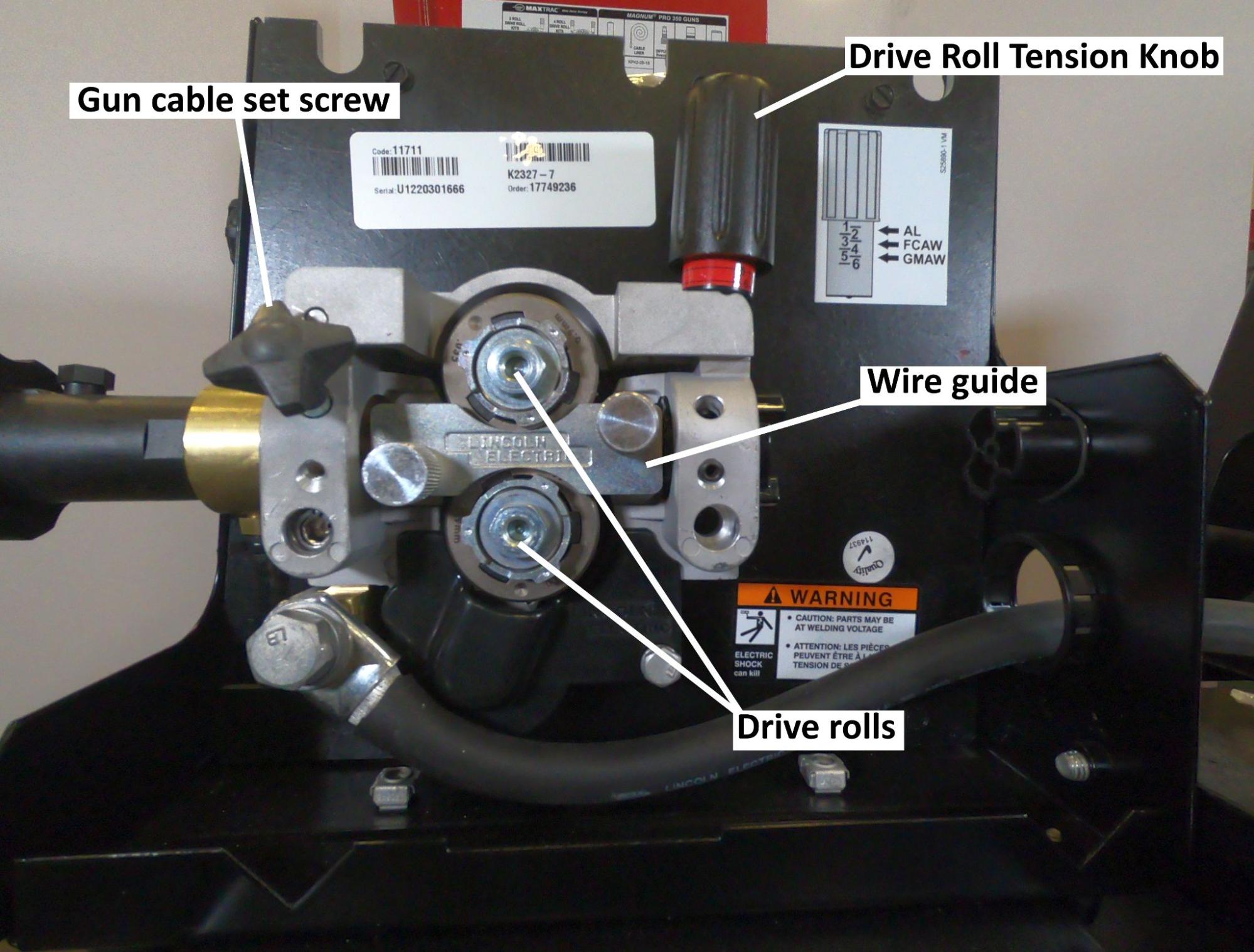 The interior of a wire feeder with major components labeled. Components include gun cable set screw, drive roles, wire guide, and drive roll tension knob.