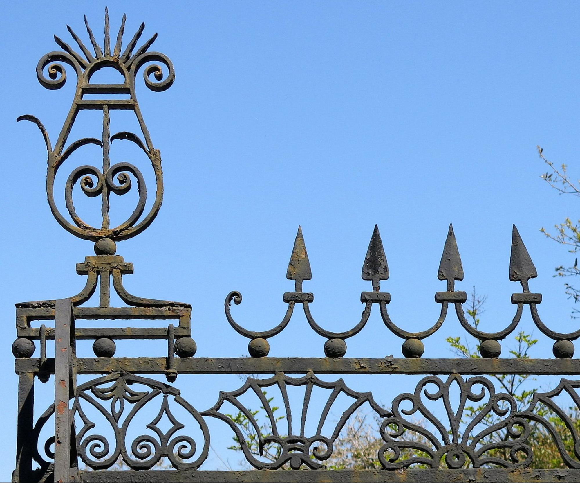 Closeup view of decorative wrought iron features such as arrowheads and stylistic peacocks on a gate.