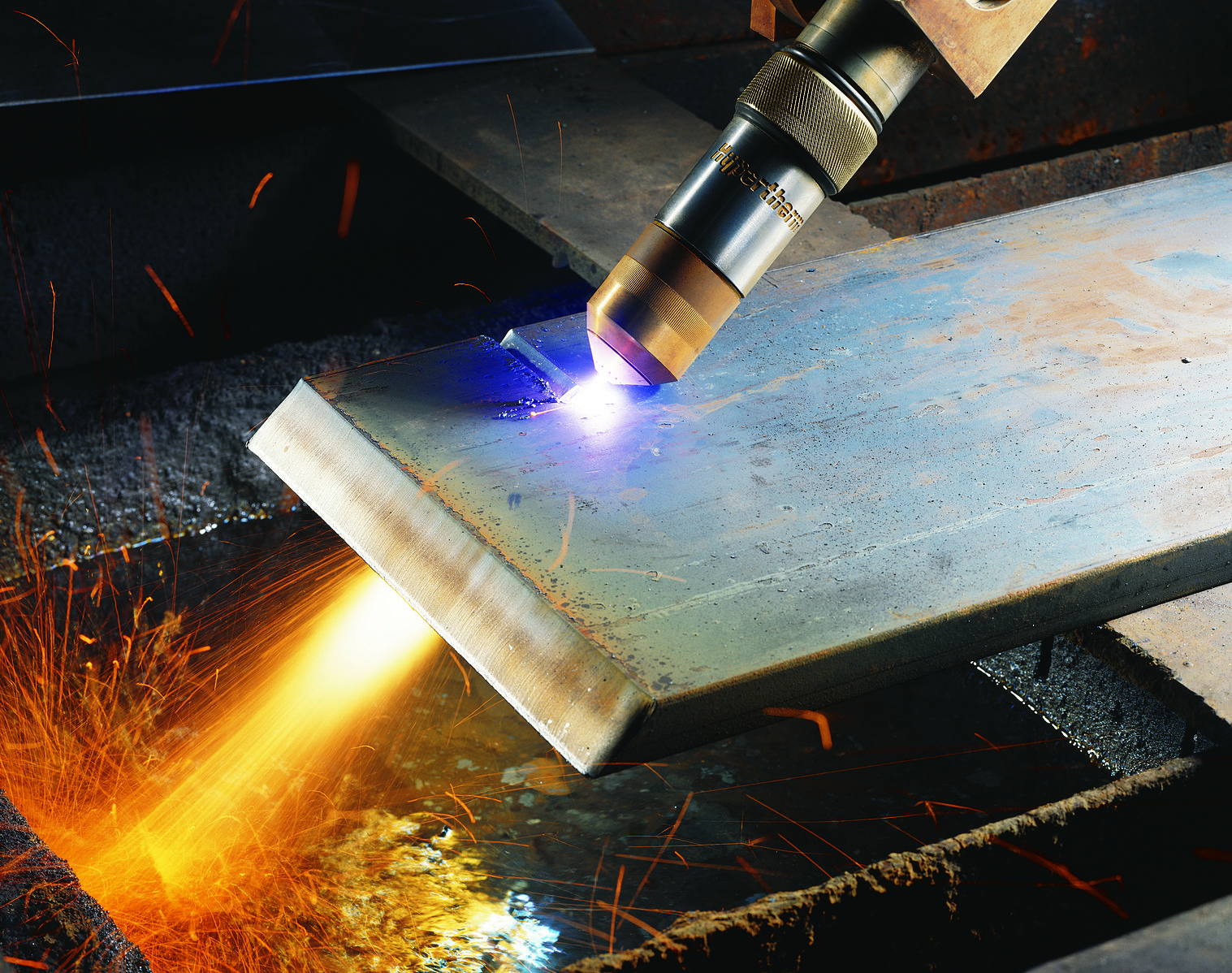 A close-up photograph of a plasma cutter, which looks like a nozzle, cutting across a piece of metal.