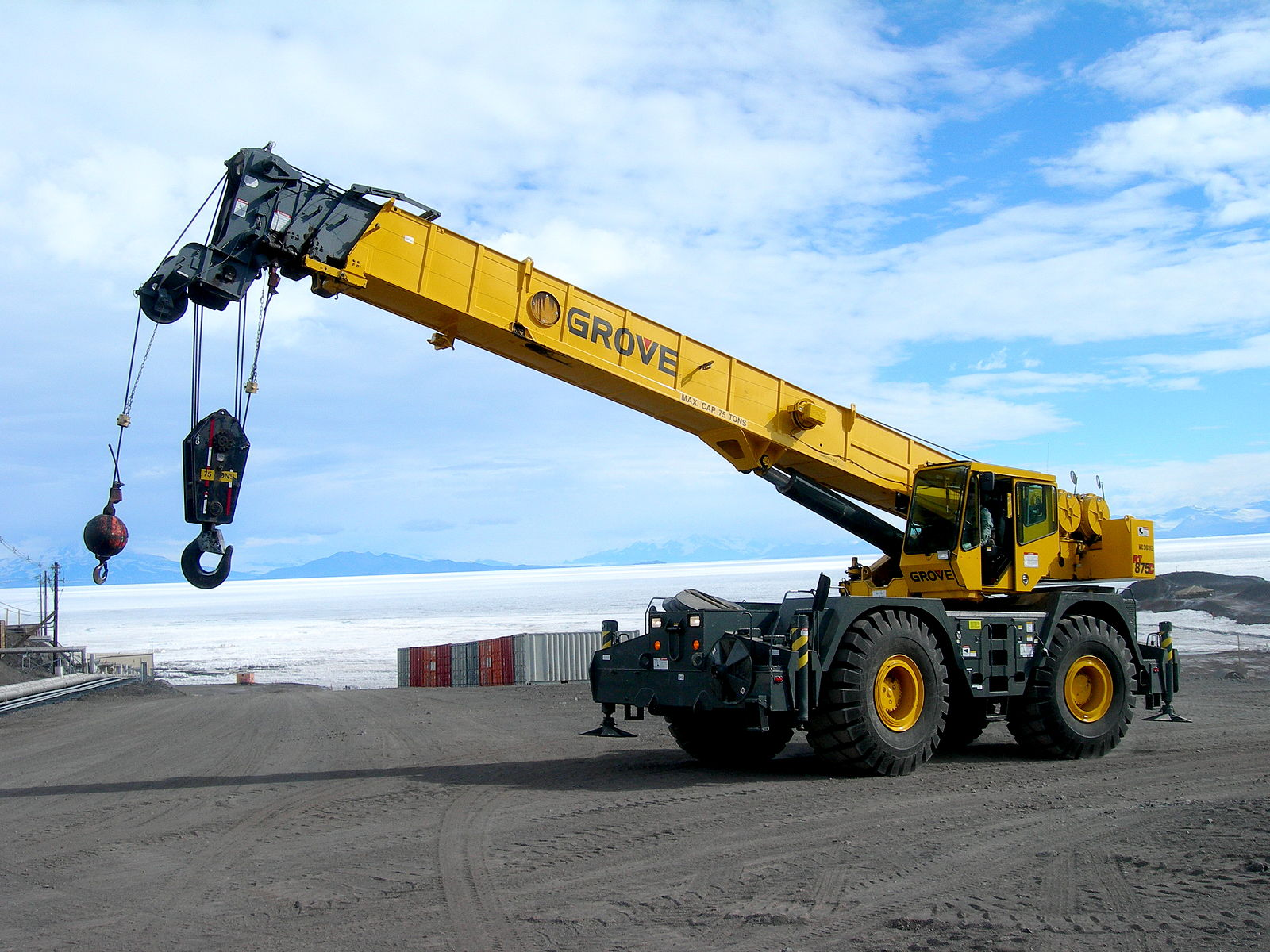 A ground crane with large tires with a lake and mountains in the background.