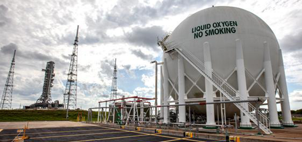 A photograph of a pressure vessel. A building-sized, white, spherical shaped structure with at least seven (the visible ones) legs holding the sphere in place. A set of stairs on the outside of the sphere lead to the top. In big letters on the sphere is written, “Liquid Oxygen - No Smoking.”