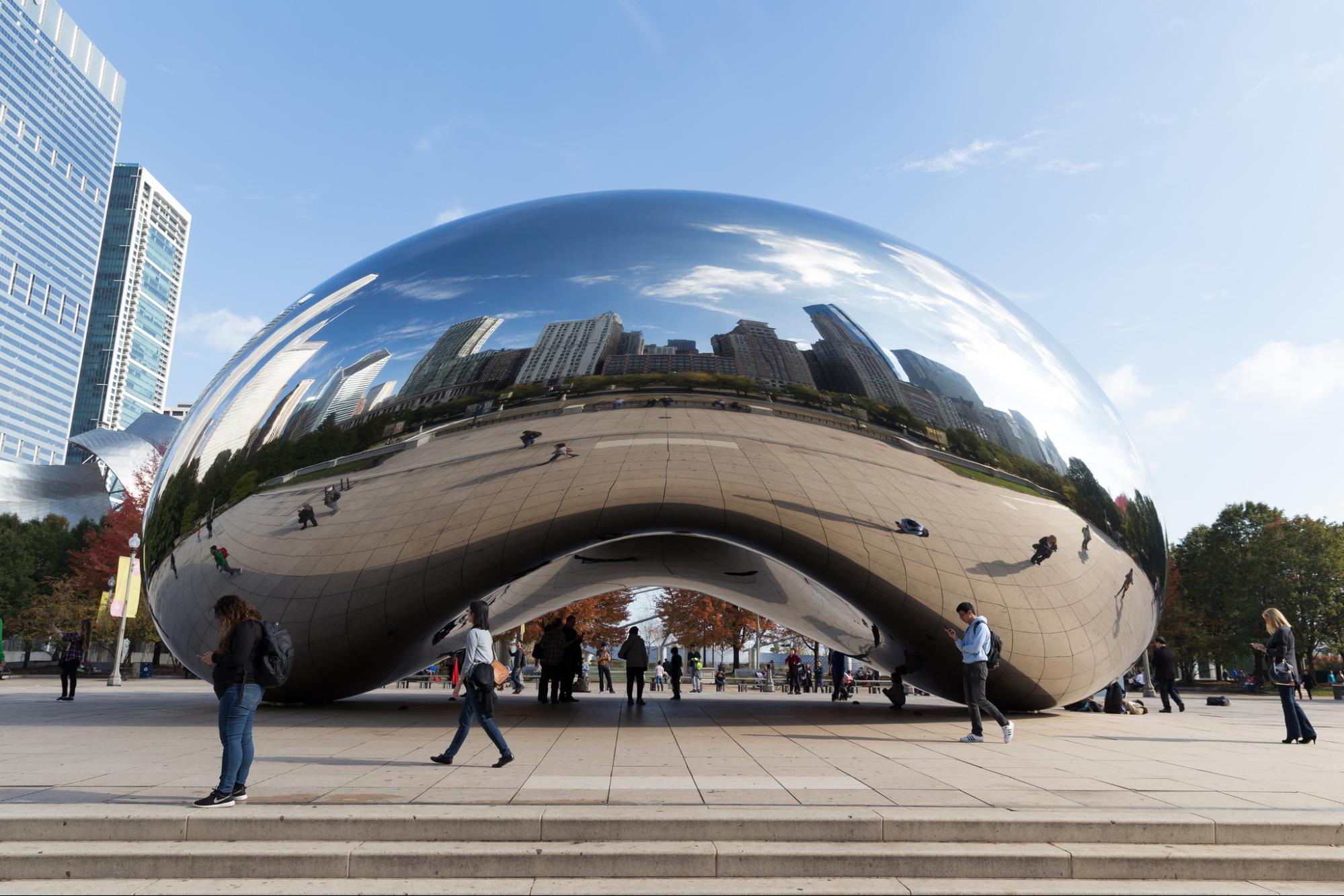 A giant coffee-bean shaped stainless steel sculpture known as Cloud Gate. People walk around and under the structure, which is placed on a wide promenade.