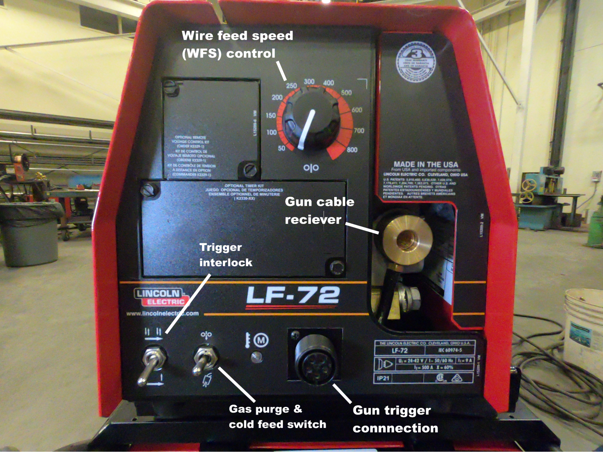 Front of a wire feeder with the major components and controls labeled. Labels say wire feed speed (WFS) control, gun cable reciever, trigger interlock, gas purge & cold feed switch, and gun trigger connection.