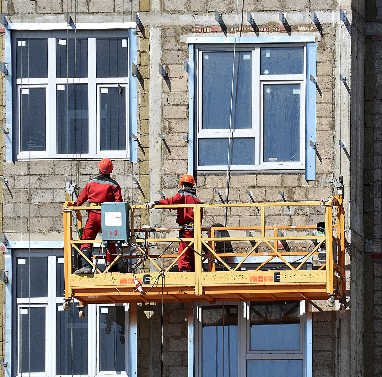 Two workers are in a swing stage platform hanging outside a building.