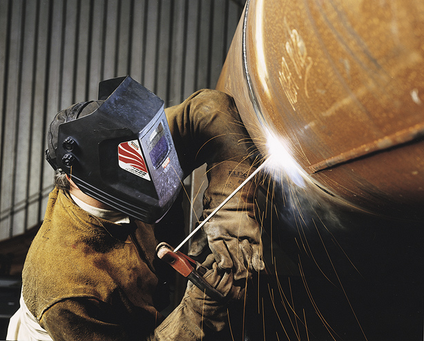 A welder using SMAW to make a weld on a large pipe.