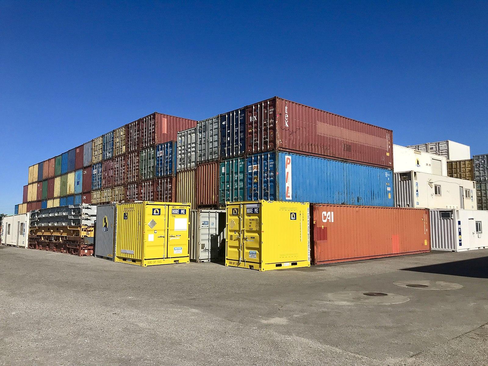 Large shipping containers of different colors are stacked in a paved lot.