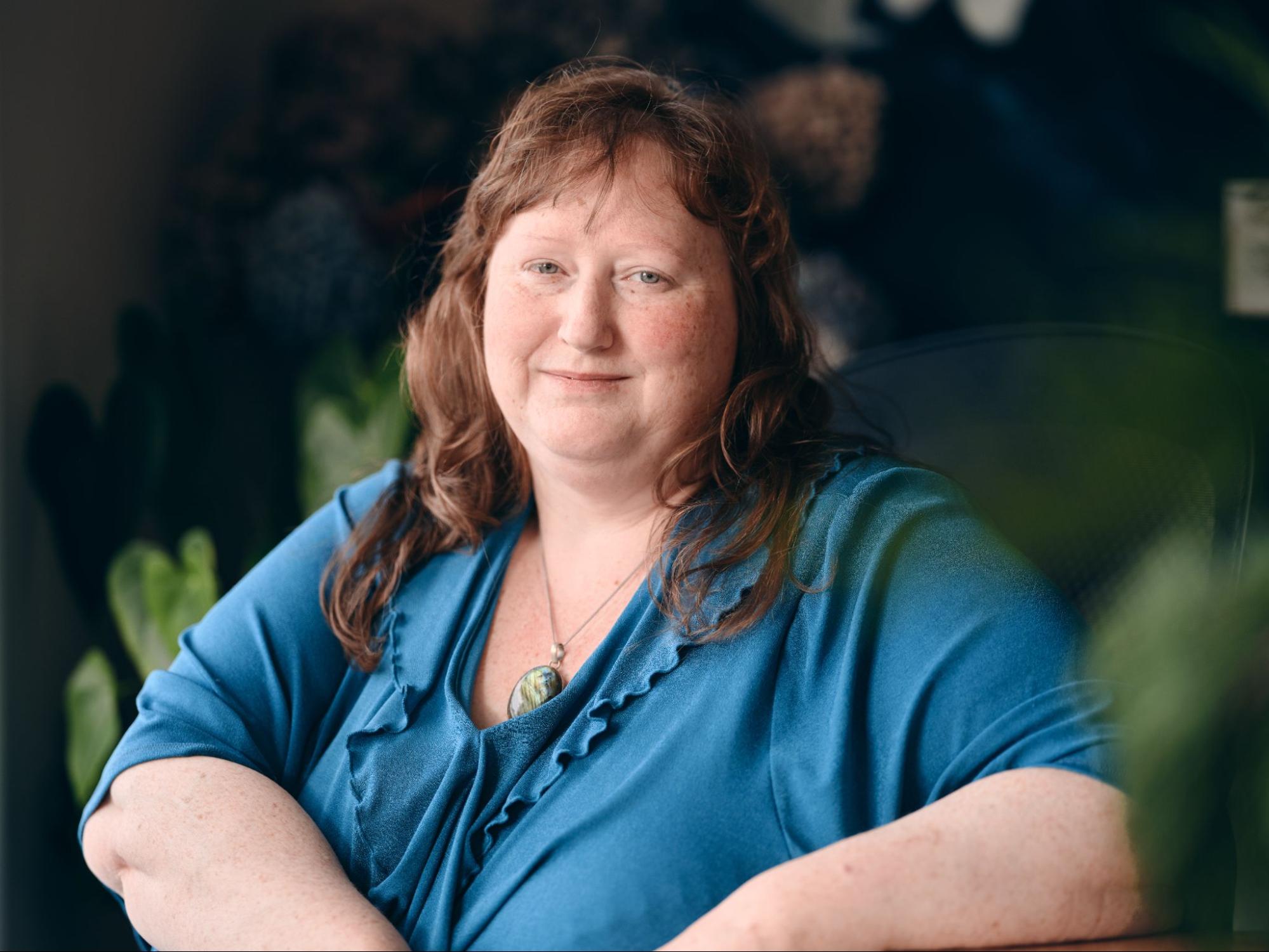 A white woman with long reddish hair and freckles is smiling.