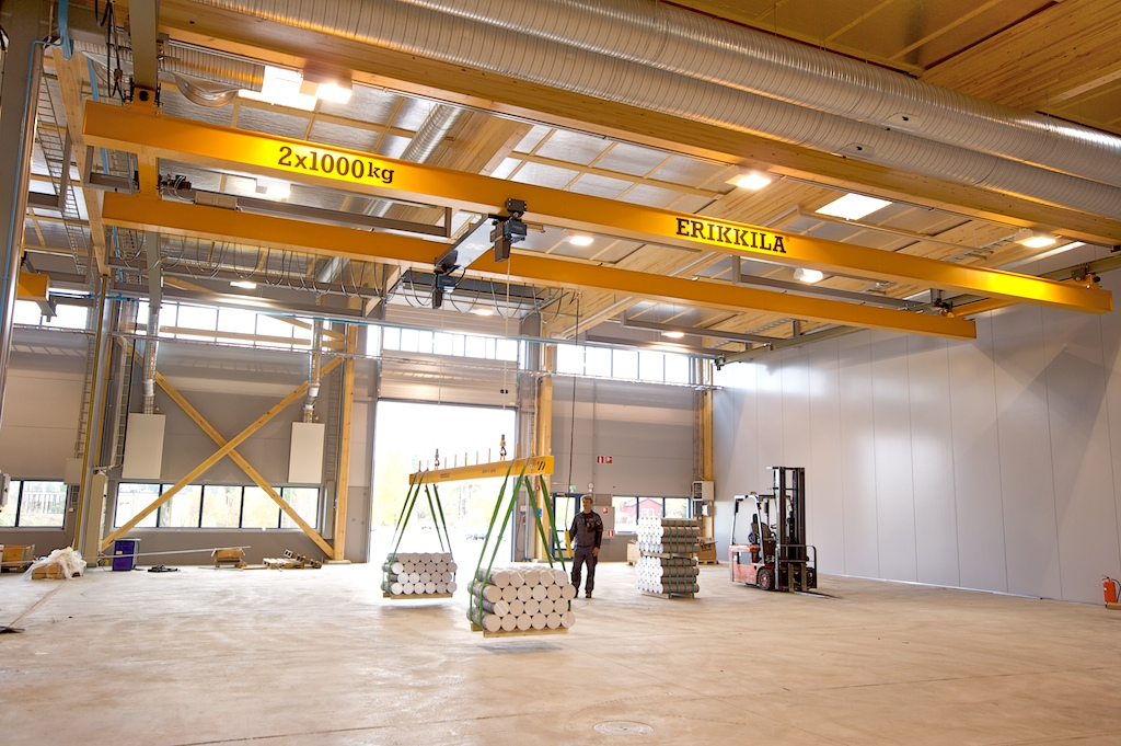 A new, empty building has an overhead bridge crane lifting a load of metal weights.