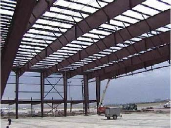 A very large open structure building made of steel beams on both the sides and top. A trailer sits on the ground in the building, but the trailer has lots of space surrounding it.