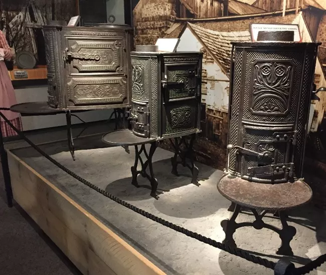 Three different style cast iron stoves on display in a museum.