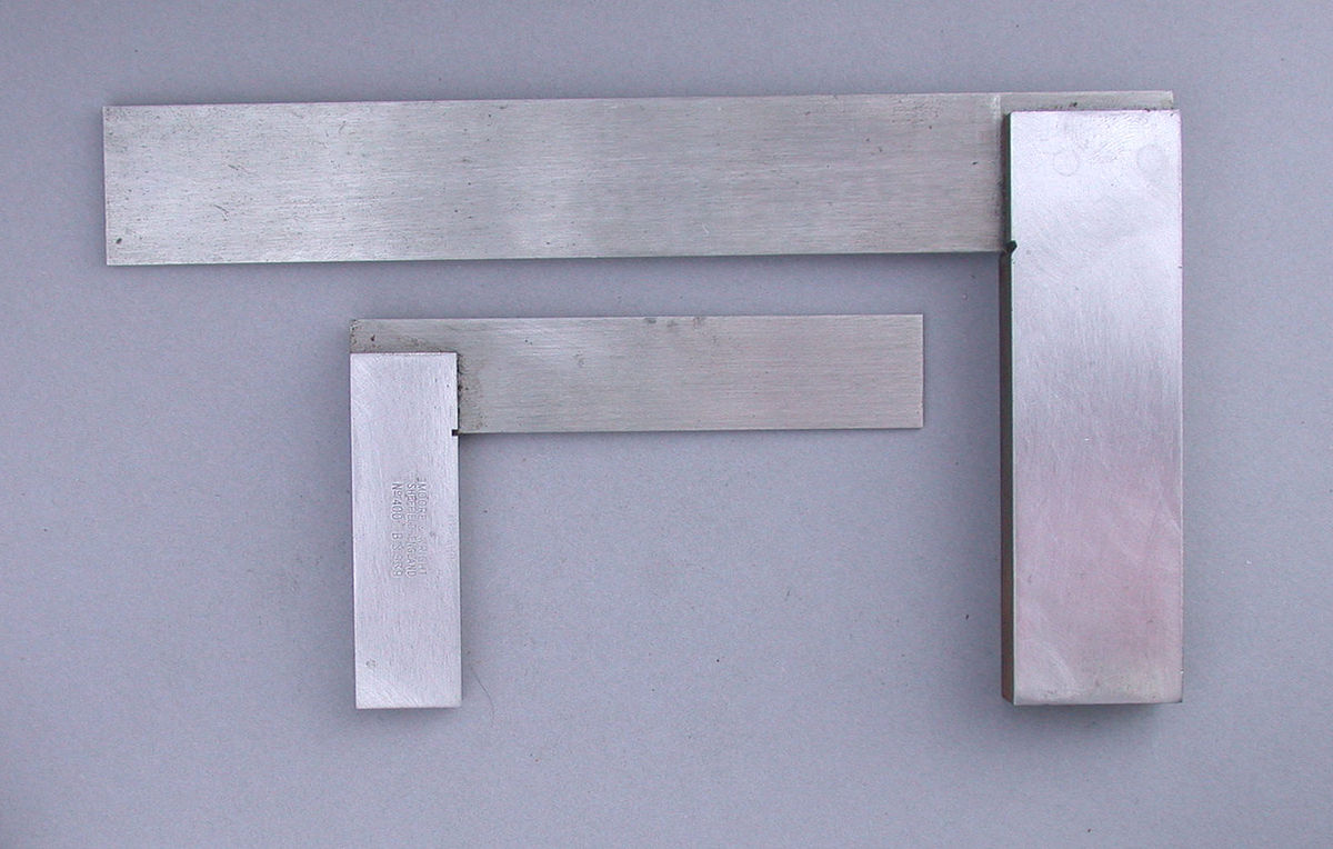 A set of machinist squares are pictured. The squares are made of a thicker metal bar welded at a 90o angle to a thinner piece of metal called a blade. In this image, there is one larger and one smaller machinist square.