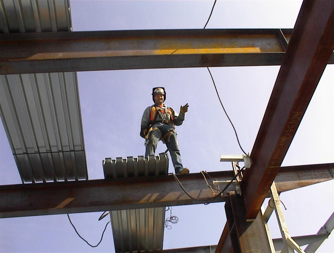 A construction welder stands atop a beam in a building under construction.