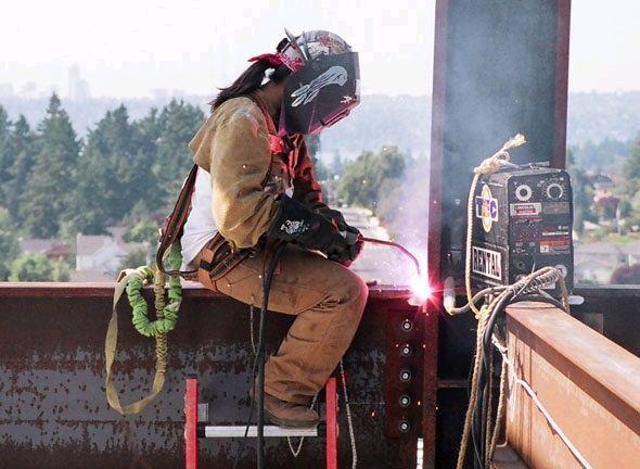 April seated on a beam in a highrise welding the beam to the column.