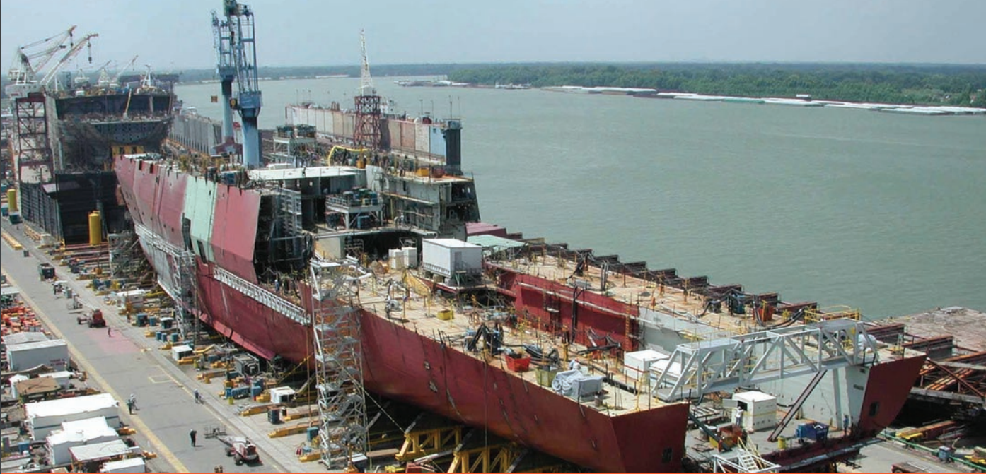 A large red ship in dry dock is being built. The ship is made of steel.