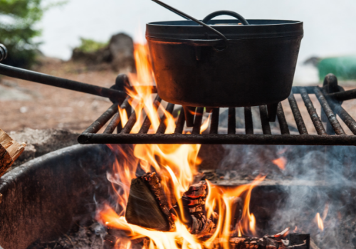 Cast iron cookware on a grate over a fire outside.