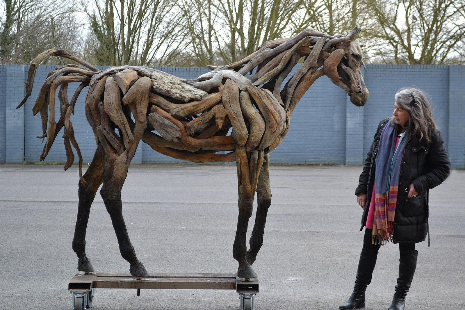 A woman stands next to a lifesize sculpture of a horse