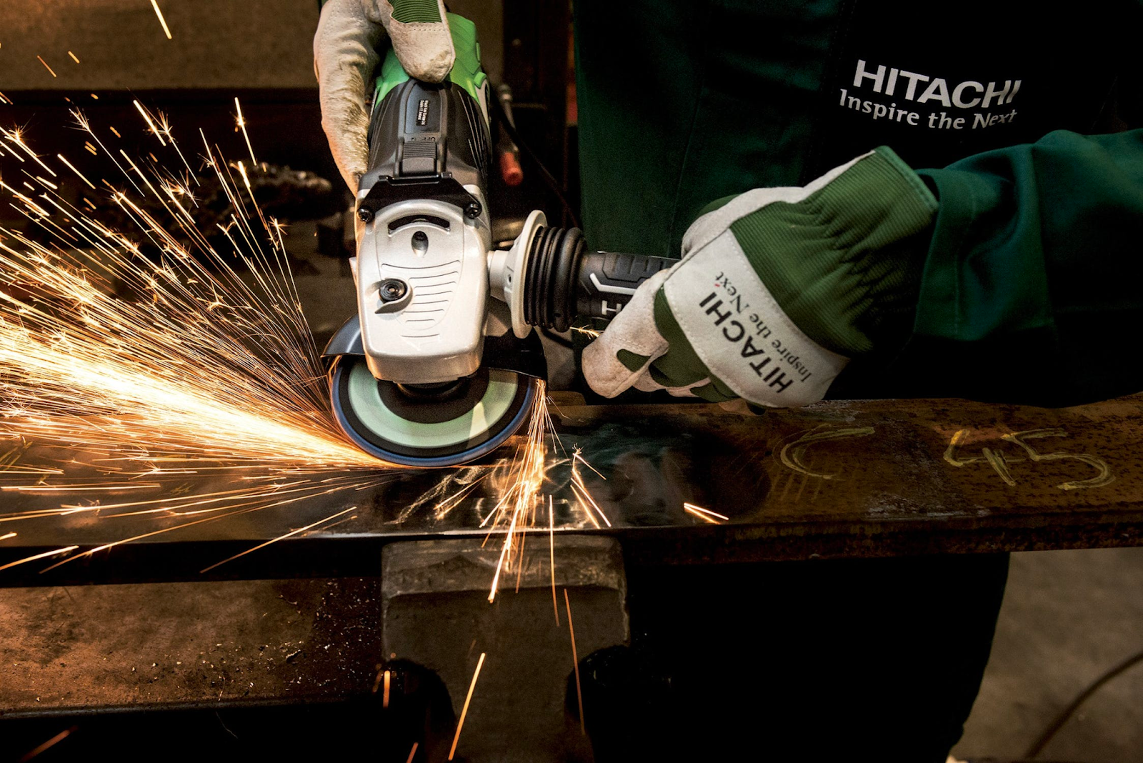 A worker uses an angle grinder to grind a piece of steel. There are many sparks flying in the air.