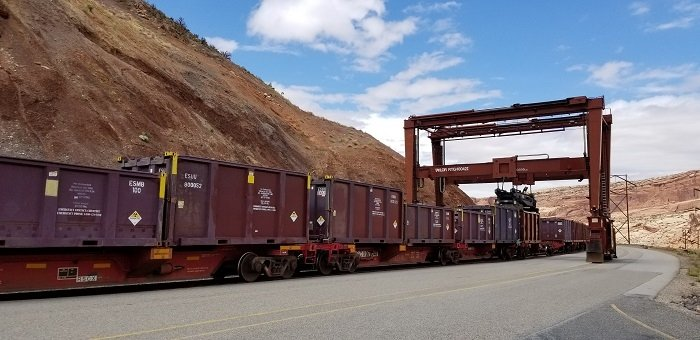 Steel rail cars sit on rail ties as they collect a load of cargo from a permanent overhead loading structure also made of steel.