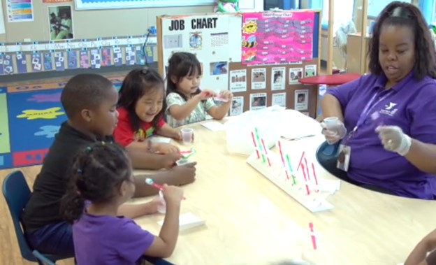 Children brushing teeth at table with teacher supervising