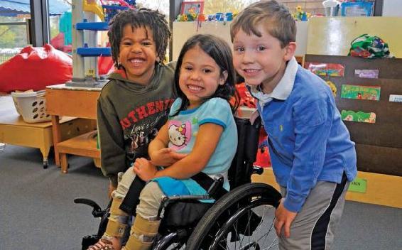 Three smiling children, one in a wheelchair.