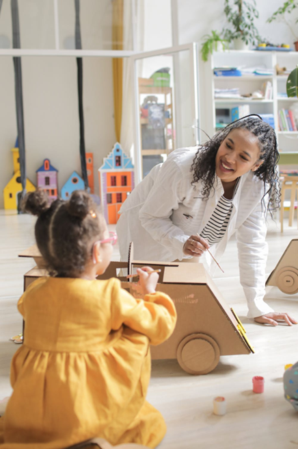 A teacher works with a child on a craft car.