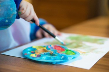 Child’s hand holding a paintbrush with a palette of paint.