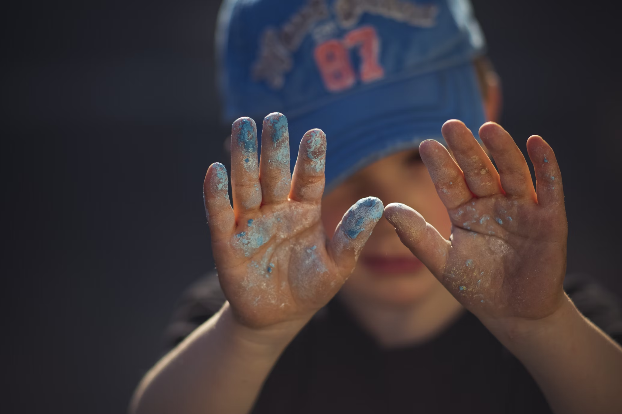 Young boy holds up hands that are covered in blue chalk.