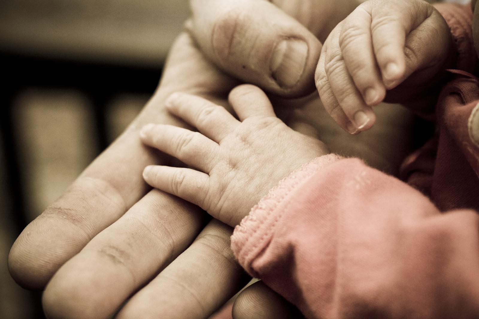 Adult holding the hands of a young child. Depicts "connection.