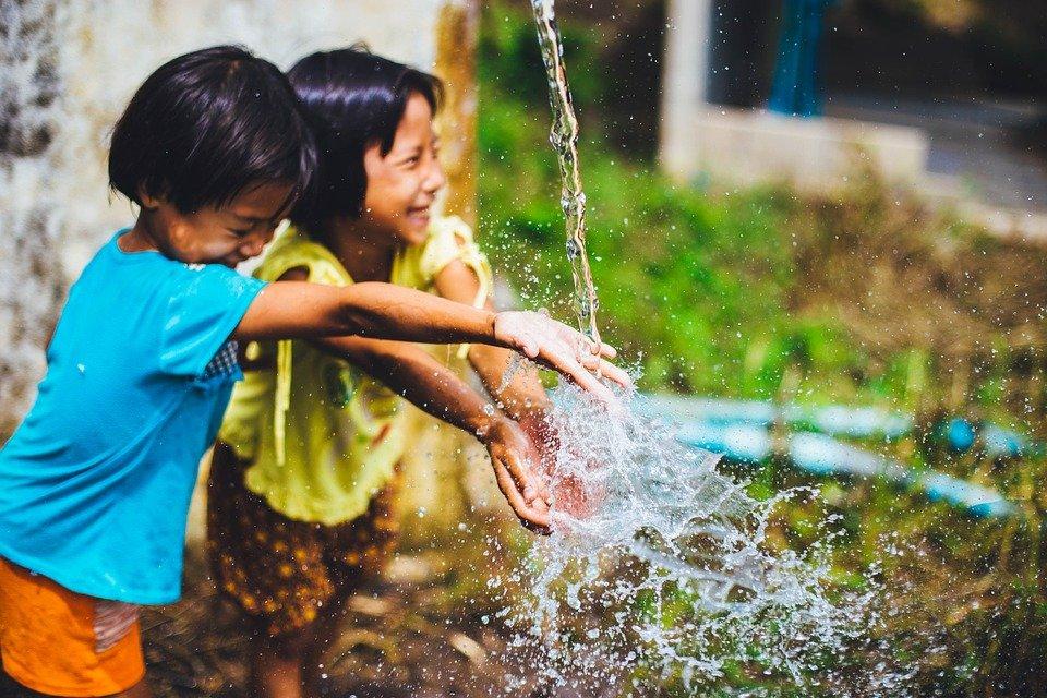 Two children with arms extended into a stream of water coming from above.