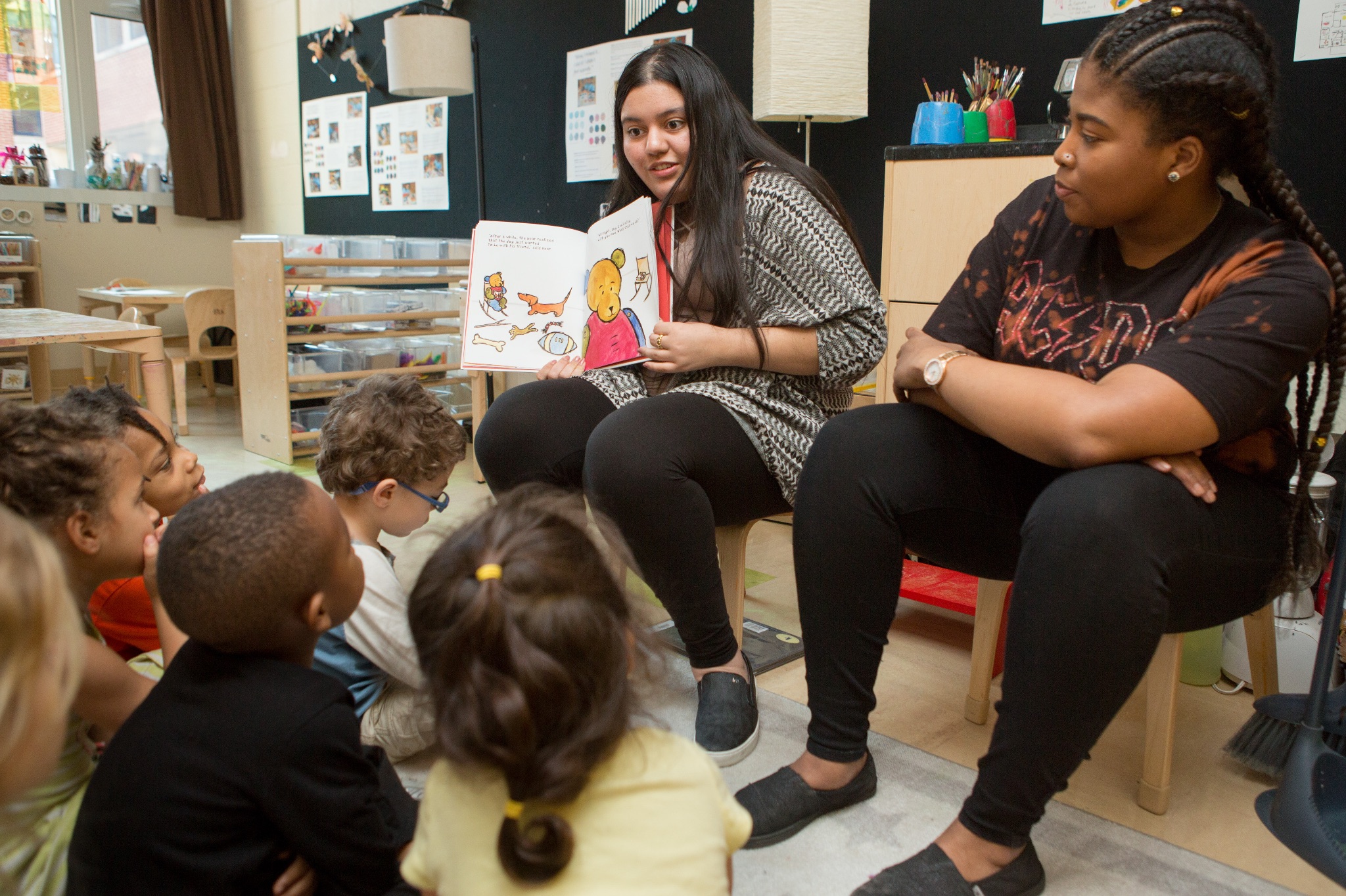 Teachers sitting with children in circle time and reading a book.