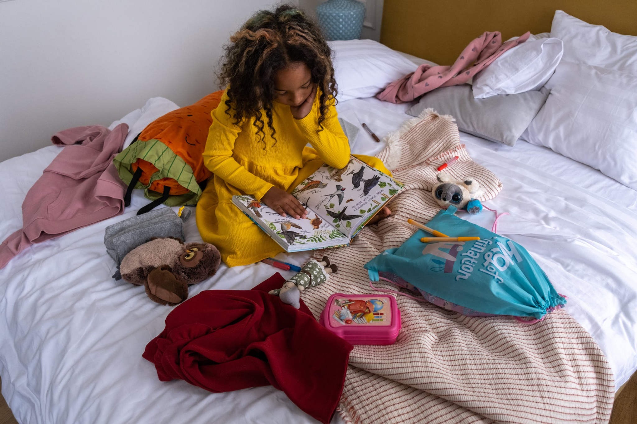 A Young Girl Sitting on the Bed while Reading a Book