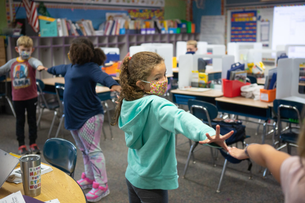 Second-grade students create distance between each other using their arms as they line up to go outside.