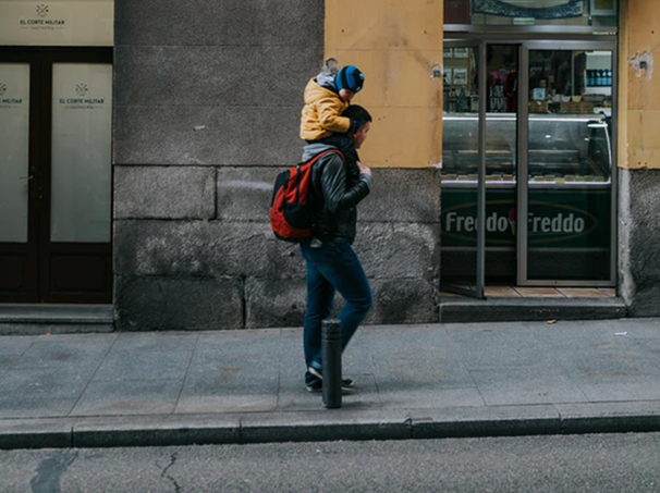 Father walking uphill with young child on his shoulders. Father is shown having a connection with the child.