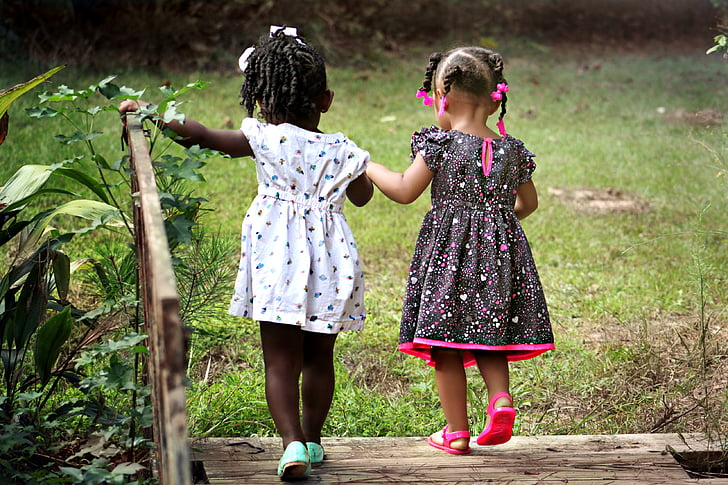 Two girls outside on a small bridge holding hands. The photo is included to illustrate positive social interactions.