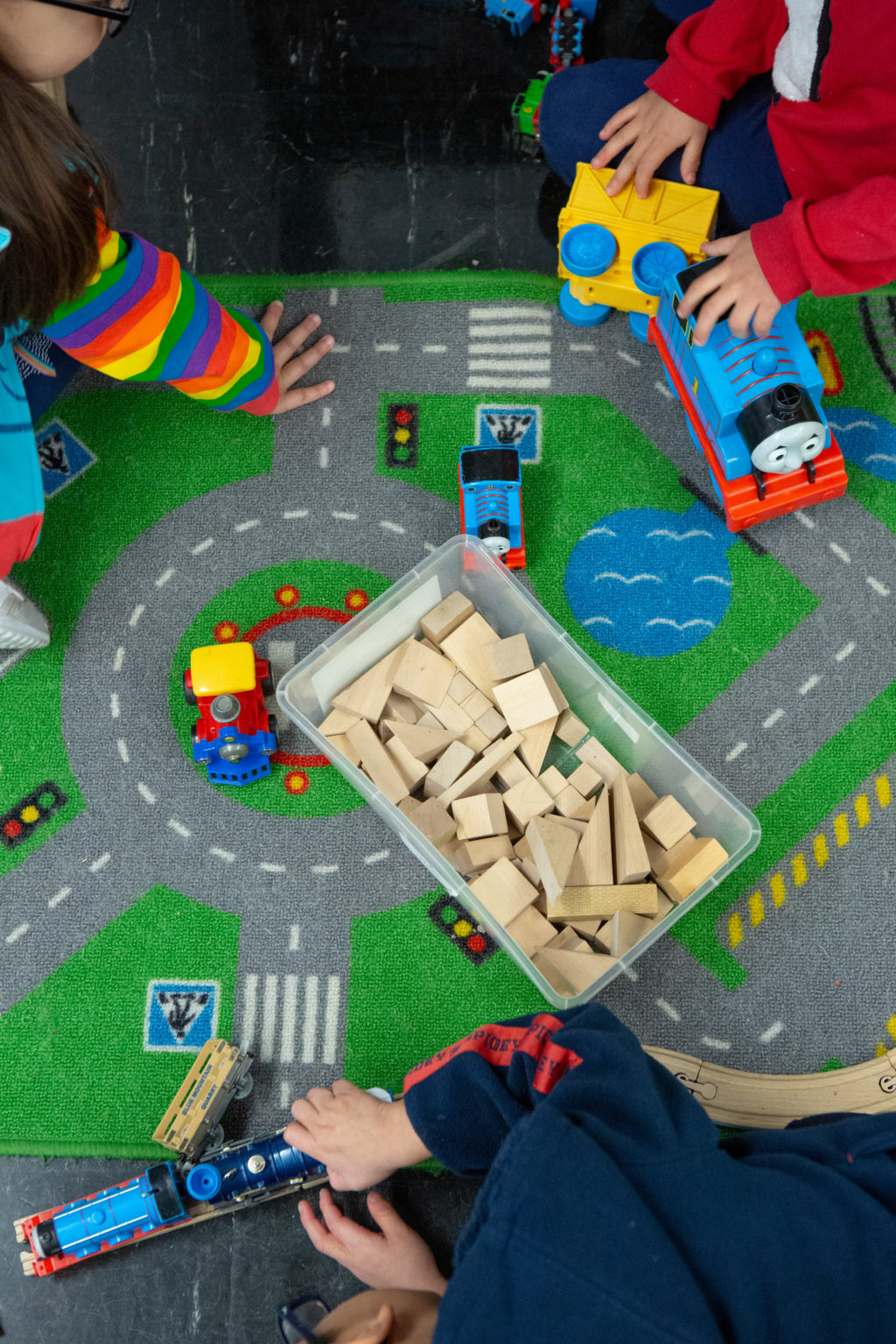 Child’s hands playing with trains, a rug with roads on it, wood blocks.