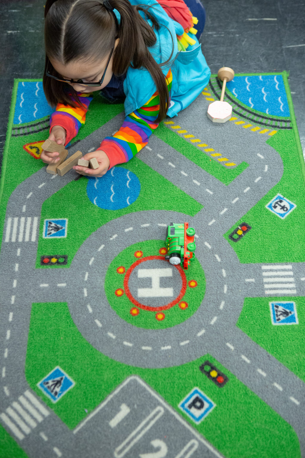 A girl playing alone with blocks on a road carpet. The inference here is that the child is alone due to the trauma she has experienced, and may not be comfortable in social interactions with others.