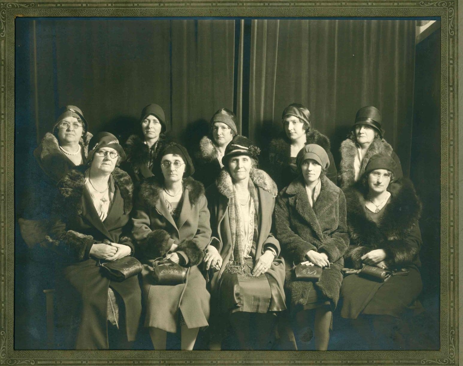 Photograph of twelve women jurors seated together with serious expressions. They are holding purses and wearing hats and overcoats with fur collars, reflecting the fashion of the time.